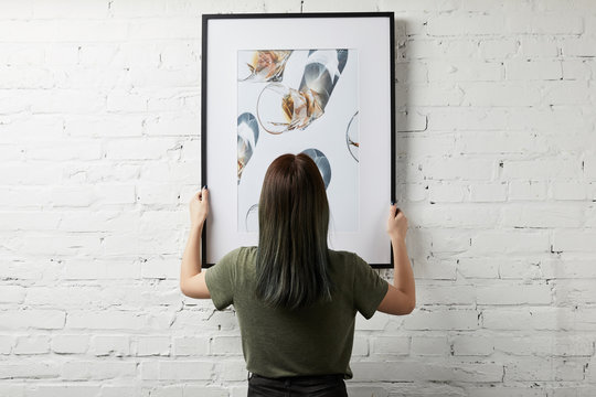 back view of woman holding drawing in black square frame