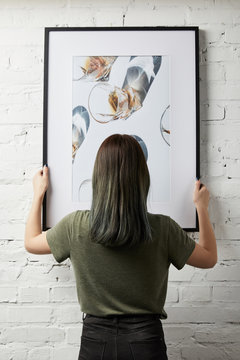 back view of woman holding drawing in black square frame in hands