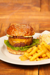Luxury beef burger in bun with cheese, bacon marmelade, lettuce, french fries and coleslaw salad