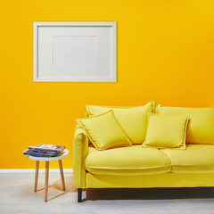 coffee table standing near modern yellow sofa near white frame hanging on wall