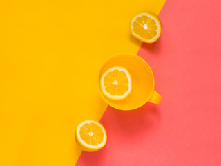 Creative fresh layout. Water with lemon in a yellow mug on a yellow and pink geometric background. Healthy drink, live water, lemonade. Biohacking minimalist concept. Flat lay