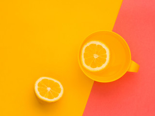 Creative fresh layout. Water with lemon in a yellow mug on a yellow and pink geometric background. Healthy drink, live water, lemonade. Biohacking minimalist concept. Flat lay