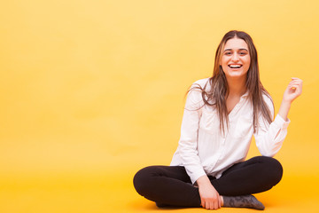 Attractive girl in white shirt smiling and sitting down over yellow background