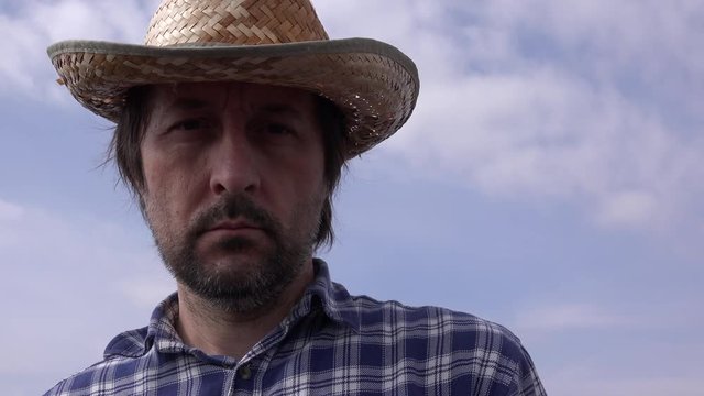 Portrait of serious farmer thinking outdoors in field, male farm worker wearing plaid shirt and straw hat is planning next agricultural activity