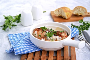 Fried chicken in a creamy garlic sauce or chkmerili chicken in a portioned ceramic pan on a light gray background. Georgian cuisine. Selective focus.