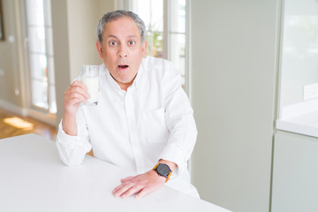 Fototapeta premium Handsome senior man drinking a glass of fresh milk at breakfast scared in shock with a surprise face, afraid and excited with fear expression