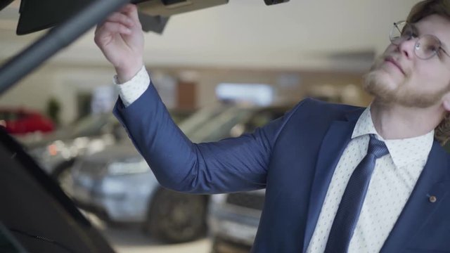 Bearded businessman choosing the car in motor show close up. Tall guy inspects the trunk of the elite vehicle. Serious man choosing automobile in motor show. Concept of buying car