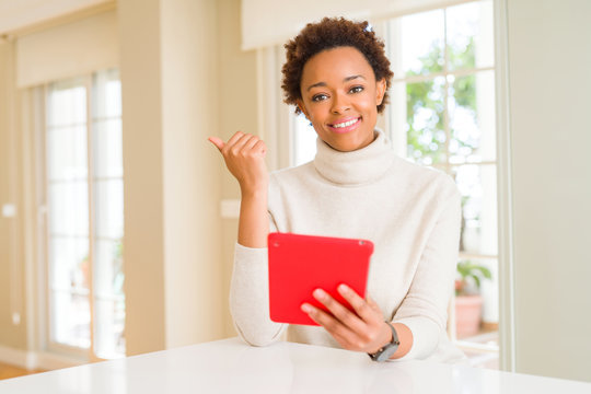 Young african american woman using tablet pointing and showing with thumb up to the side with happy face smiling