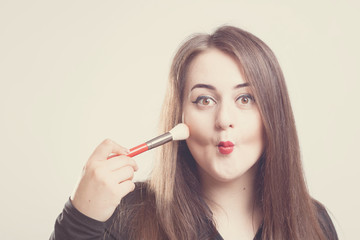 Obraz premium Model plus size with sweet donut, happy smiling girl posing with cosmetic, doing makeup for her self with brush in black bodysuit. XXL female on light background with space for text