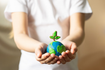 A small globe with trees in the hands of a child. Layout of the planet made of plasticine in...
