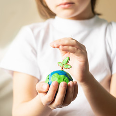 A small globe with trees in the hands of a child. Layout of the globe made of plasticine in...