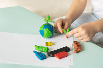 The child sculpts from plasticine the globe and trees. Layout of the planet in children's palms. Concept ecology.