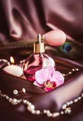 Vintage spray atomizer perfume bottle and pearl jewellery on silky dark pink fabric with peacock...