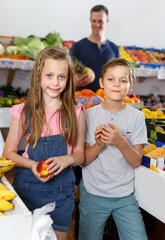 Preteen children choosing delicious fruits, parent on background