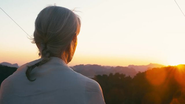 Rear view of undefinable elderly woman with gray hair waching sunset on a summer evening.