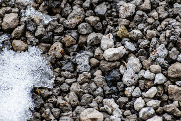 Gray gravel of different shapes, cold stones in winter and the remains of white snow. Natural background and texture