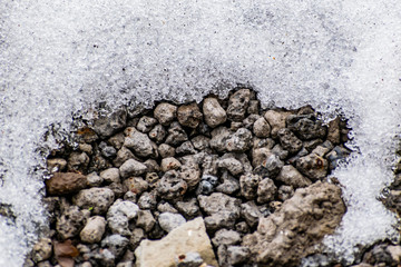 Gray gravel of different shapes, cold stones in winter and the remains of white snow. Natural background and texture