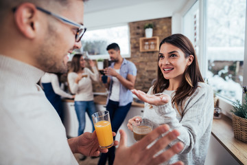 Millennial friends standing in the kitchen, drinking coffee and orange juice and talking on winter day.