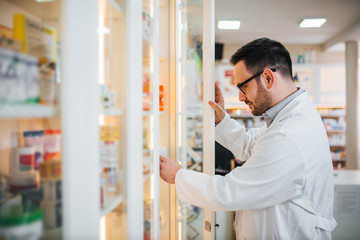 Naklejka na ściany i meble Pharmacist checking for medicine in shelf at pharmacy.
