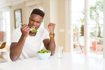African american man eating fresh healthy salad annoyed and frustrated shouting with anger, crazy and yelling with raised hand, anger concept