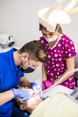Male dentist and female assistant checking up patient teeth with dental tools microscope, mirror...