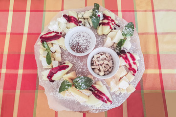 cheese plate with apples, honey and cashews, different types of cheese sprinkled with jam and sprinkled with powdered sugar, bowl of cashews, top view
