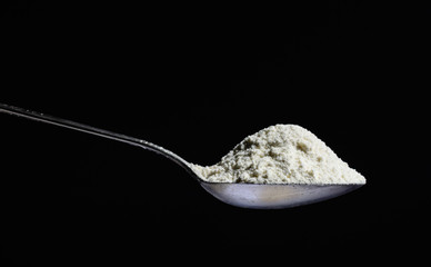 Metal silver spoon with the flour in it. Large side view. Black dark background. Plenty of room for text.