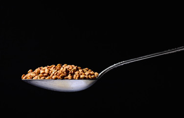 Metal silver spoon with the buckwheatin it. Large side view. Black dark background. Plenty of room for text.