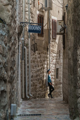 A girl stands in a narrow street in an old European city with a cobbled road and stone walls.