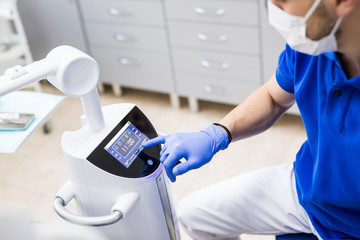 Fototapeta premium Man hand in gloves starting a teeth whitening machine. Newest Laser Dental Bleaching.