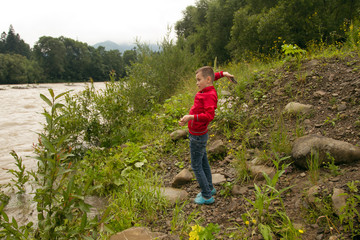 Boy Throw Stones In The River. Boy in red Jacket Throws Stones
