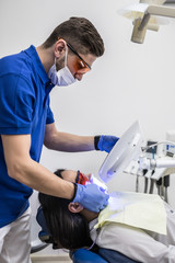 Close-up portrait of a female patient at man dentist in the clinic. Teeth whitening procedure with ultraviolet light UV lamp.