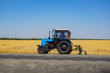 Tractor mows grass near the field. The farmer planted a vegetable garden. The endless fields of Russia in the Rostov region on the background of the highway.