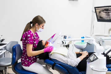 Close-up portrait of female patient at woman dentist in the clinic. Teeth whitening procedure with ultraviolet light UV lamp.