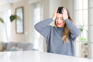 Young beautiful woman wearing winter sweater at home suffering from headache desperate and stressed because pain and migraine. Hands on head.