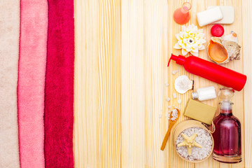 Items for spa concept, bath towels, shower gels, sea salt, soap, candle, seashells. On wooden background, top view.
