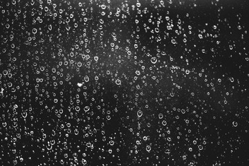 Naklejka na ściany i meble Dirty window glass with drops of rain. Atmospheric monochrome dark background with raindrops. Droplets and stains close up. Detailed transparent texture in macro with copy space. Night rainy weather.