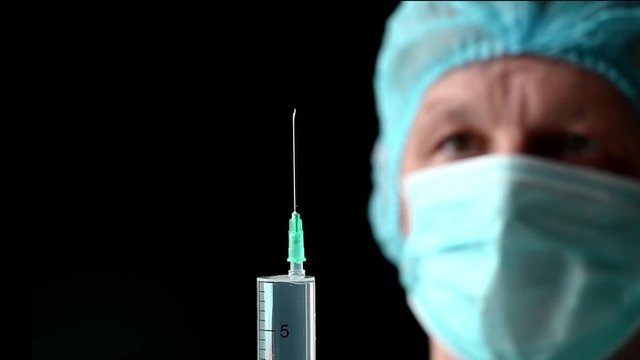 Man Doctor with syringe is preparing for injection on black.