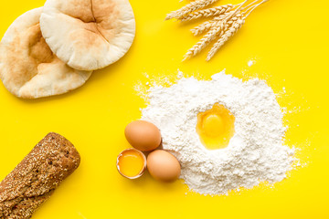 Make bread concept. Bread near wheat ears, flour and eggs on yellow background top view