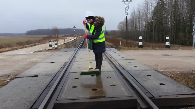 Woman railway employee clean with brush railway crossing