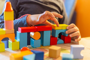 a child plays with colored wooden blocks at home.kid plays and builds buildings and towers with wooden colored blocks.