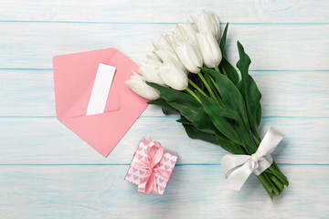 A bouquet of white tulips with a gift box, love note and color envelope on blue wooden boards