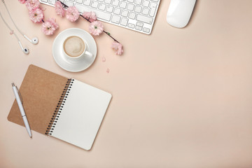 White cup with cappuccino, sakura flowers, keyboard, alarm clock, notebook on a pastel pink...
