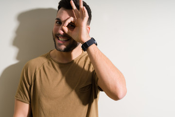 Naklejka premium Young handsome man over isolated background with happy face smiling doing ok sign with hand on eye looking through fingers