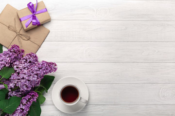 A bouquet of lilacs with cup of tea, gift box, craft envelopes, a love note on white boards