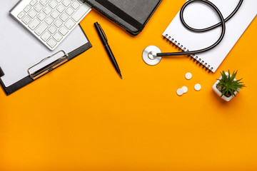 Top view of doctor's desk with stethoscope keyboard notepad and pen, prescription and pills