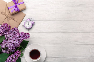 A bouquet of lilacs with cup of tea, alarm clock, gift box and craft envelope on white boards