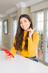 Young woman using red smartphone sending a message very happy pointing with hand and finger to the side