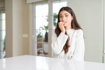 Young beautiful woman at home on white table looking stressed and nervous with hands on mouth biting nails. Anxiety problem.