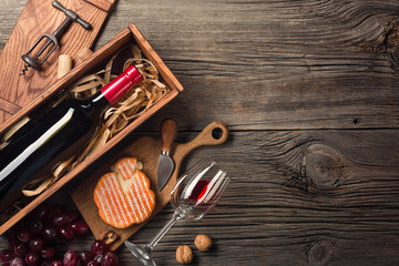 Red wine in a box with a glass, corkscrew and cream cheese on a wooden old table. Top view with...